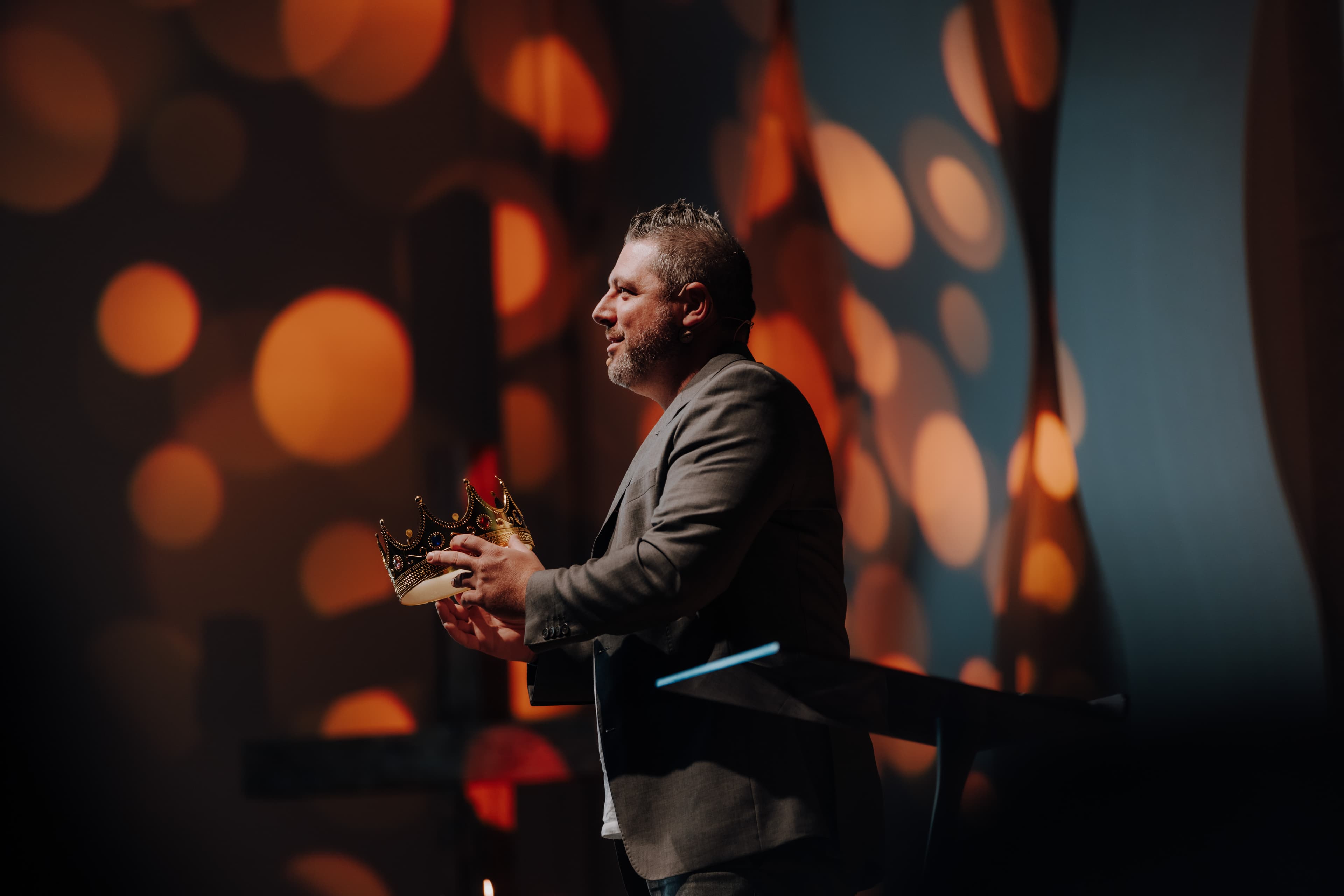 Pastor Andreas Roth from GEC Heilbronn stands on stage, holding a crown in his hand and preaching about God's kingdom.